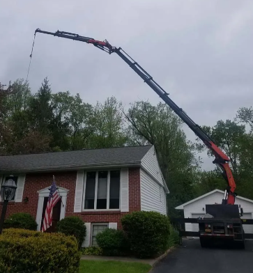 Crane truck lifting a boom over a red brick house in a suburban yard.