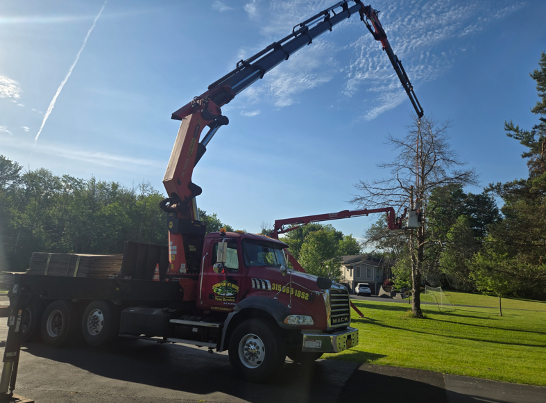 Red tow truck with extended crane parked by a grassy roadside under a sunny blue sky