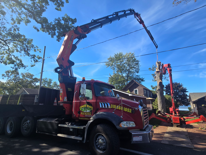 Red truck with crane arm lifting debris beside a house and utility poles under blue sky