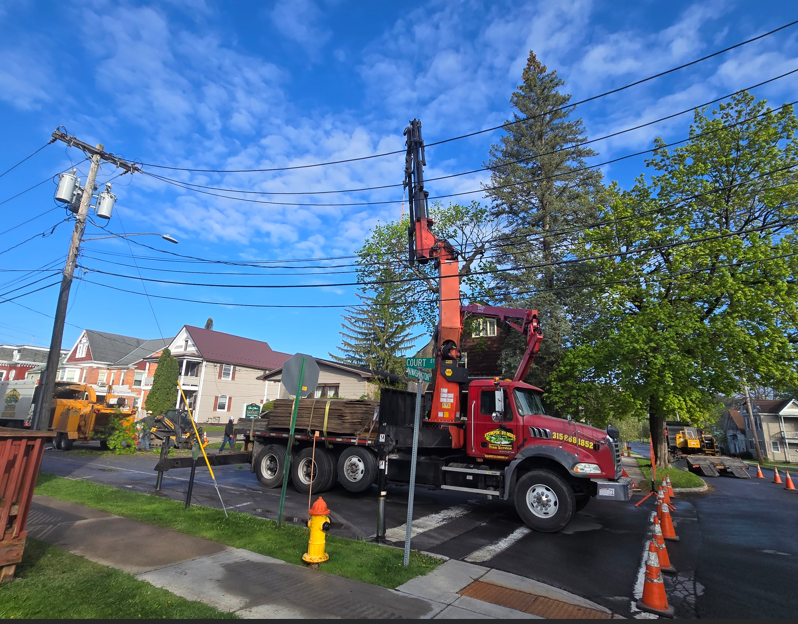 Red utility truck and crane working on roadside near a suburban intersection, with orange cones and a fire hydrant.