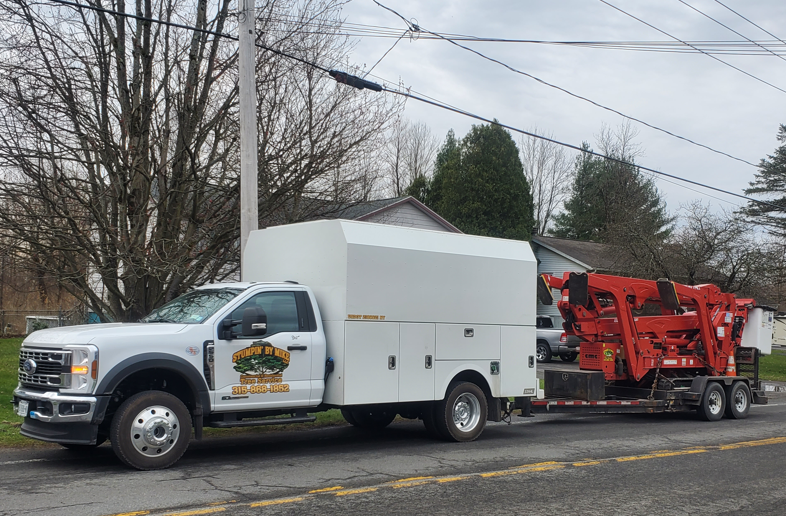 White utility truck hauling red equipment trailer on a roadside under cloudy sky