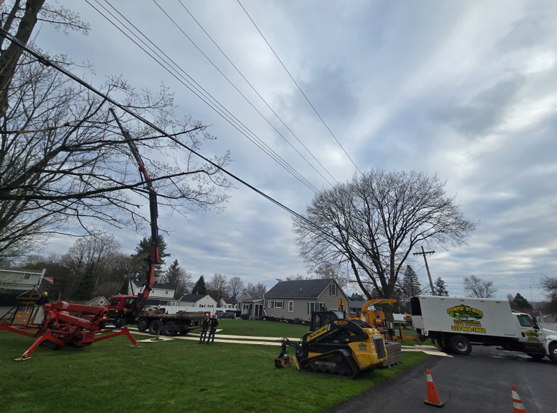 Utility workers and trucks repairing overhead power lines on a suburban street under cloudy skies