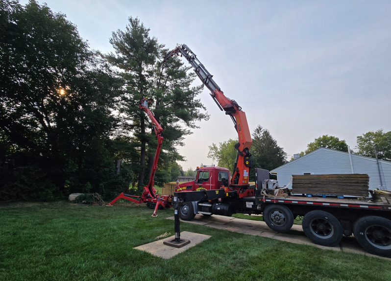 Red crane truck lifting a tree beside a house at dusk