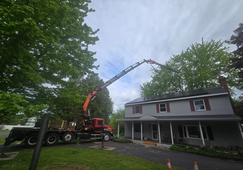 Tree-removal truck with extended boom beside a gray house on a cloudy day
