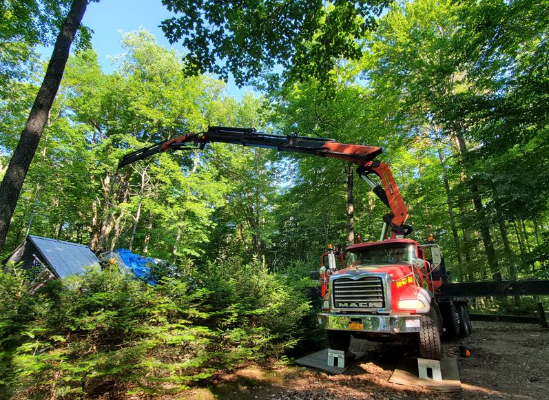 Red forestry truck with crane lifting debris in a green wooded area
