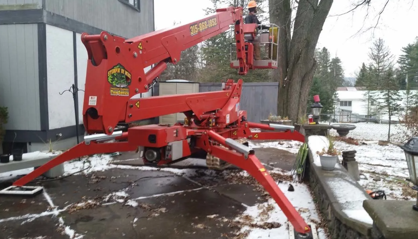 Red boom lift parked on a snowy driveway beside a building and trees.
