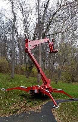 Red hydraulic aerial lift on outriggers in a wooded area