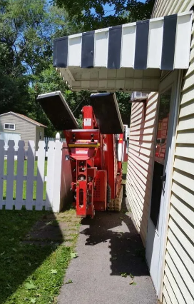 Red compact machine parked in a narrow side yard beside a house and white fence