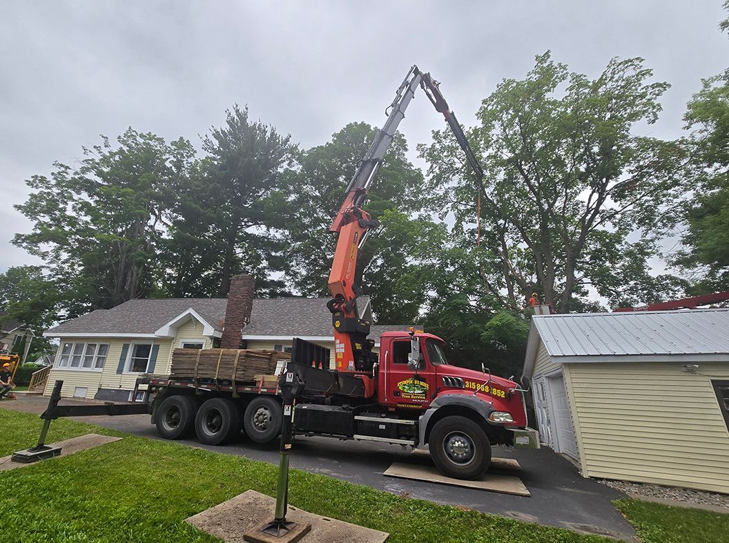 Red utility truck using boom saw to trim tree beside a house on a rainy residential street