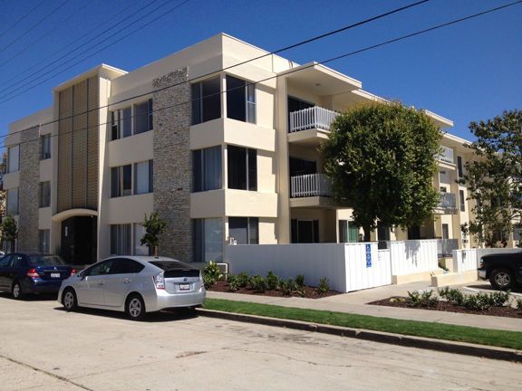 A white car is parked in front of a large apartment building