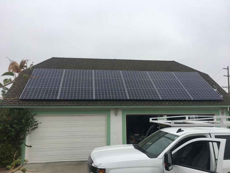 A white truck is parked in front of a garage with solar panels on the roof.