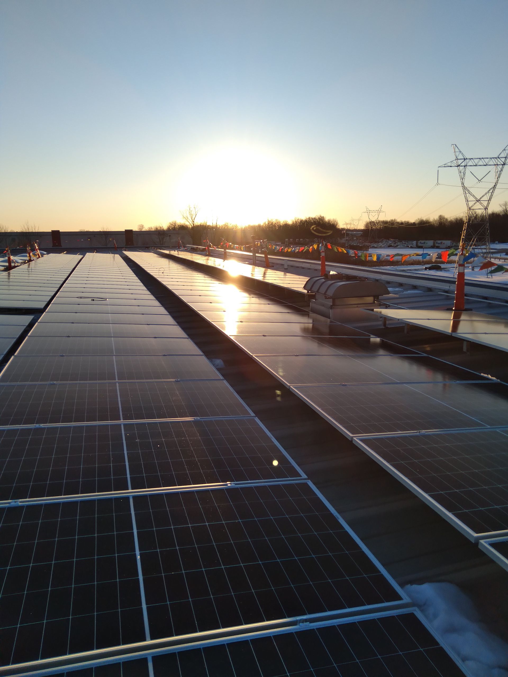 Rows of solar panels at sunrise, with bright light reflecting off the surfaces and distant power lines against the sky.