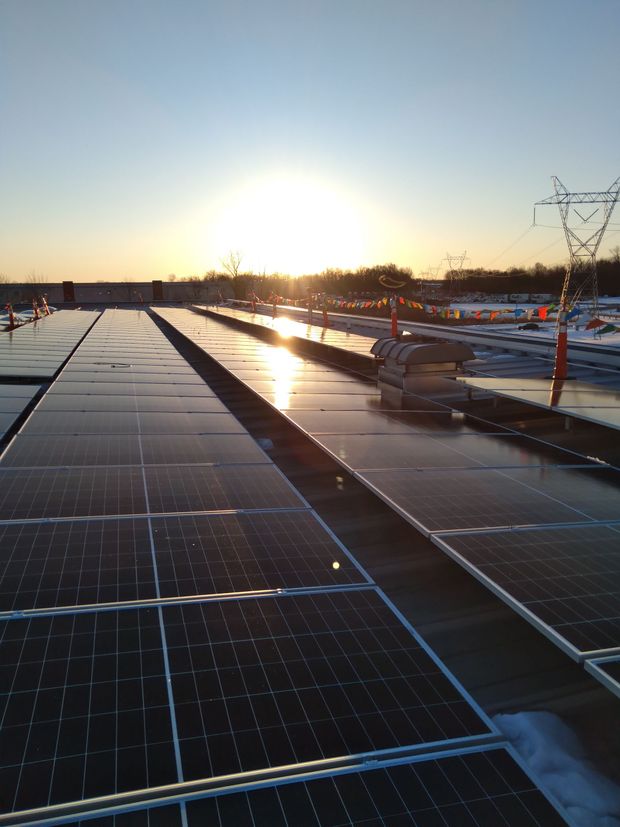 Rows of solar panels on a rooftop at sunrise with melting snow visible on the edges.