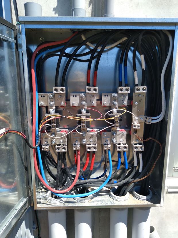 Open electrical distribution cabinet showing multiple black, red, blue, and white wires connected to metal bus bars.