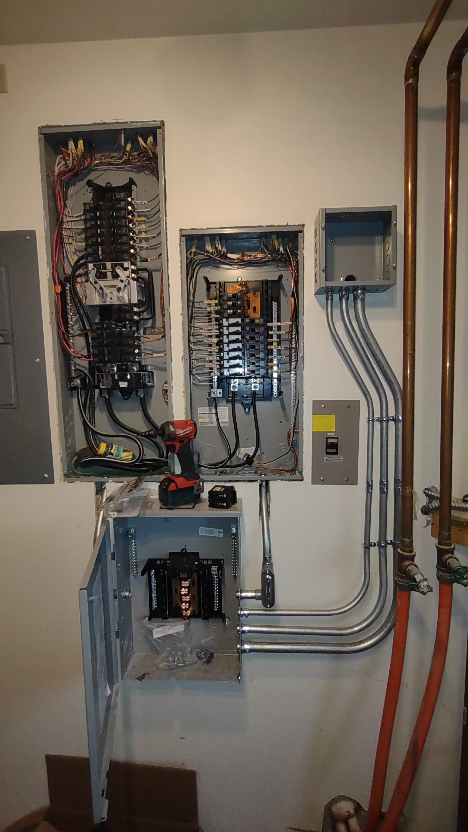 Electrical installation in progress featuring open circuit breaker panels, metal conduits, and wall-mounted electrical boxes.