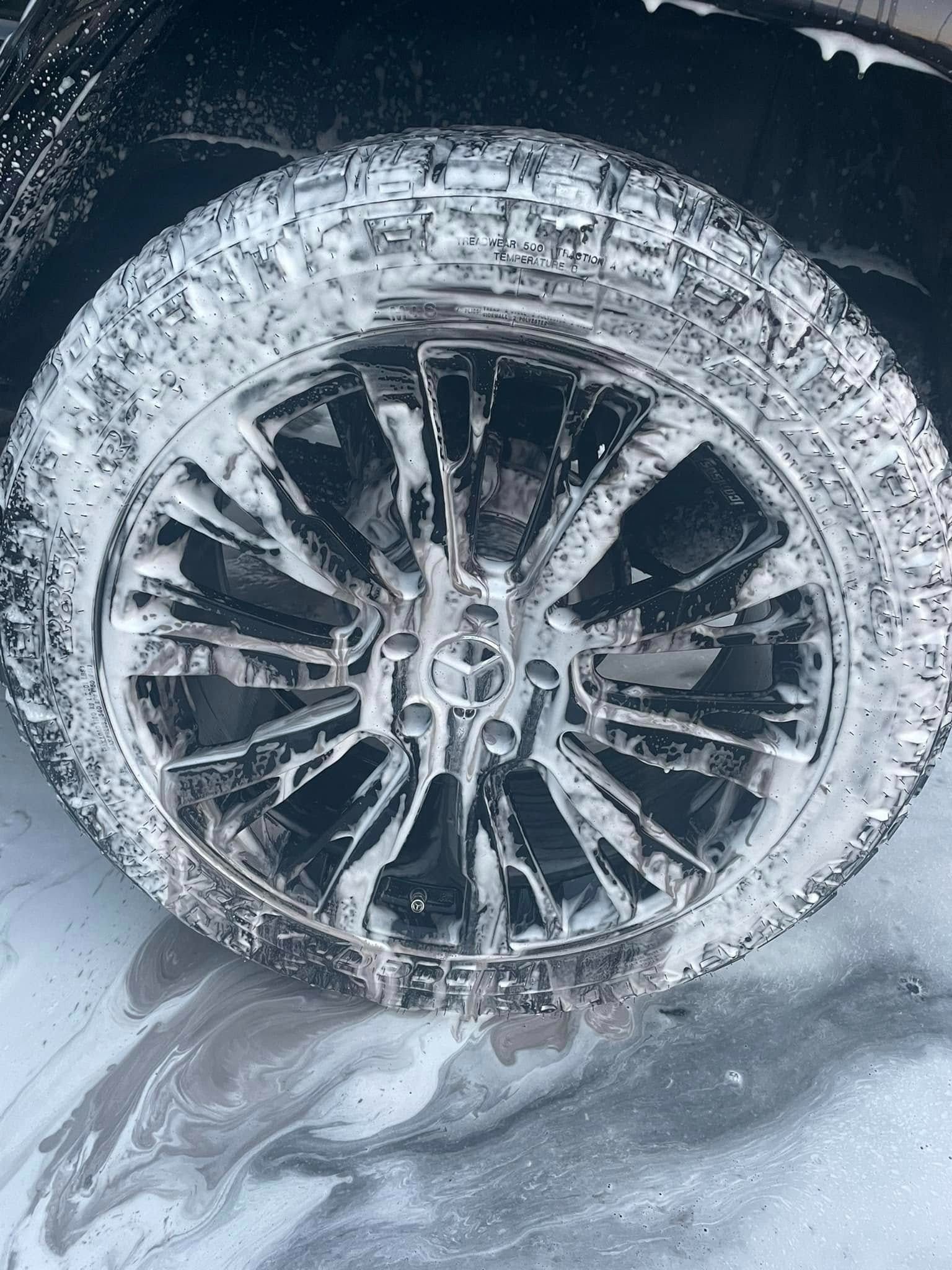 Car wheel covered in soapy foam during washing.