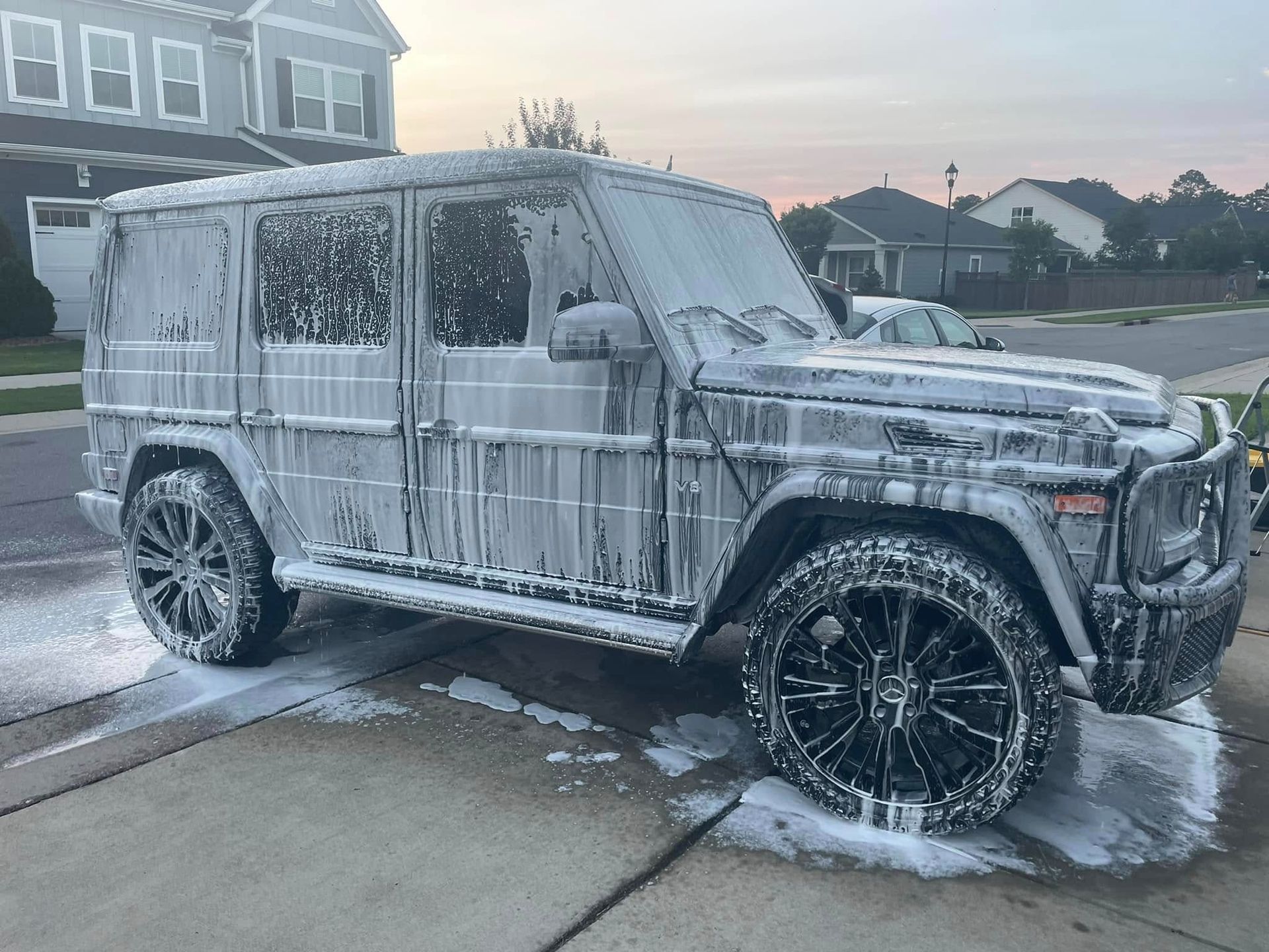 Black Mercedes G-Wagon covered in white soap suds on a driveway, being washed.