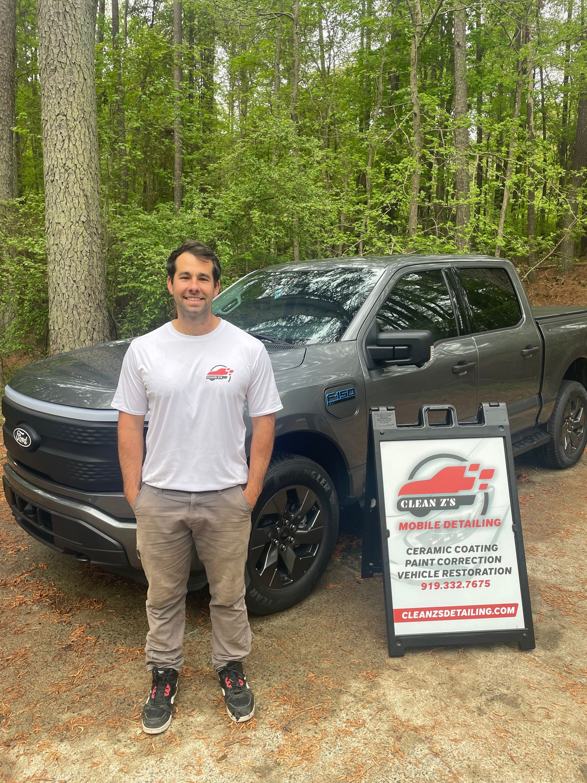 Man standing beside a grey electric pickup truck, smiling, near a sign.