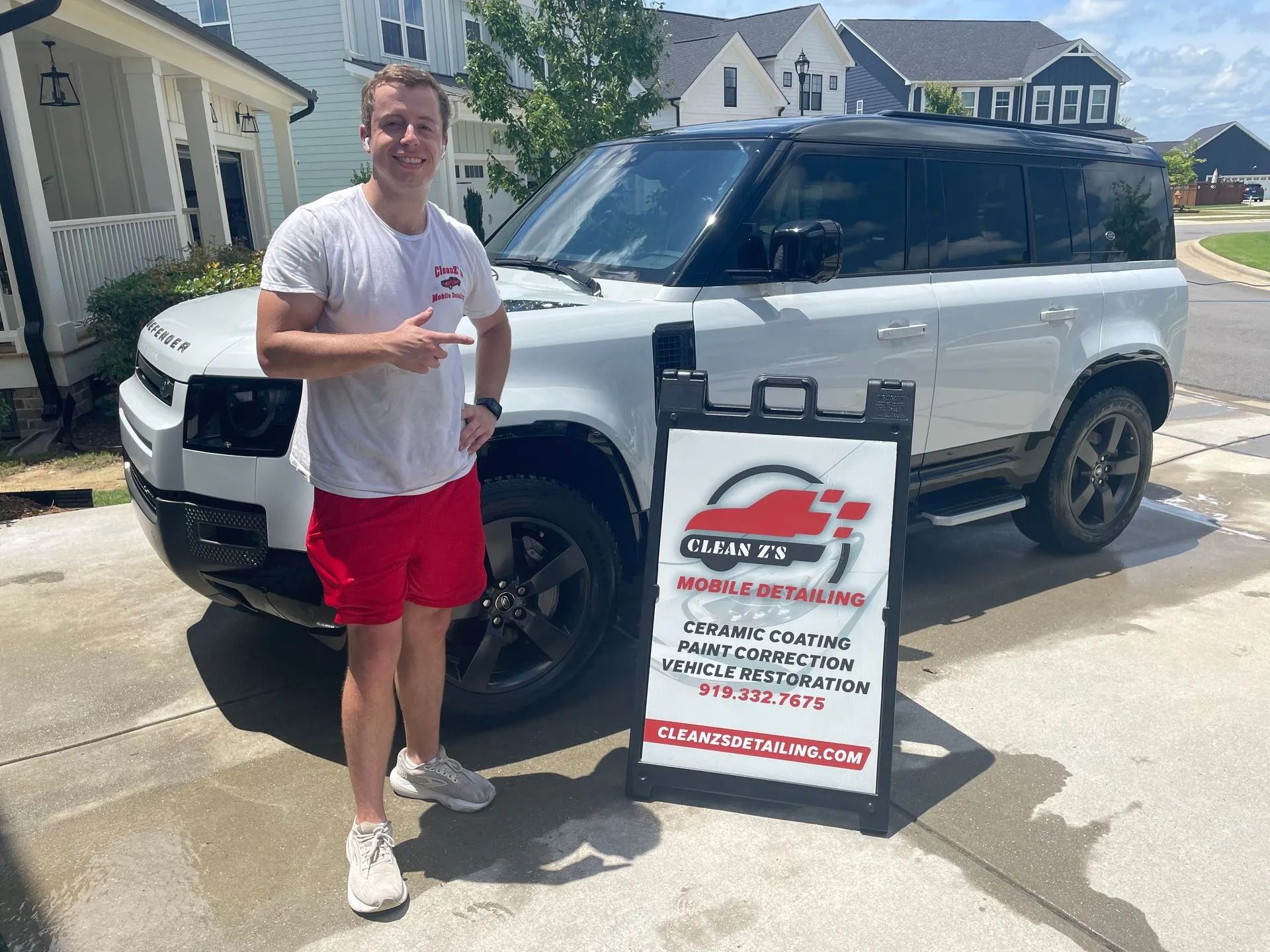 Man in red shorts by white Land Rover. Sign for 