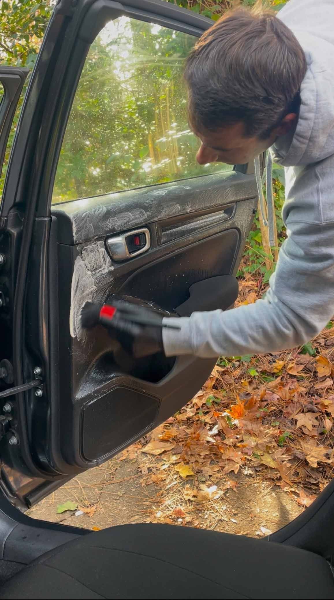 A person wearing gloves cleaning a car door in an outdoor setting.
