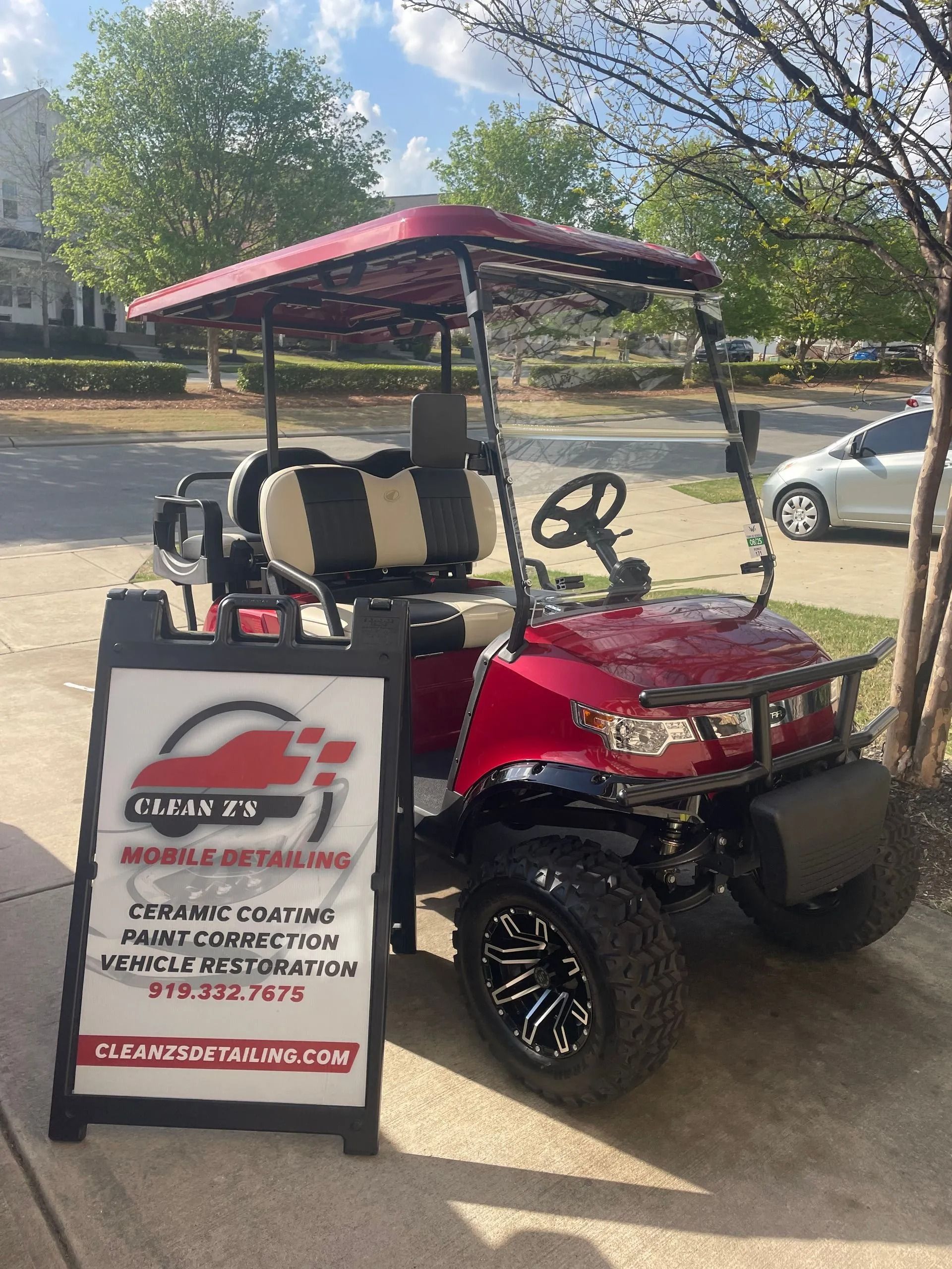 Red golf cart parked near an A-frame sign for a car detailing business.
