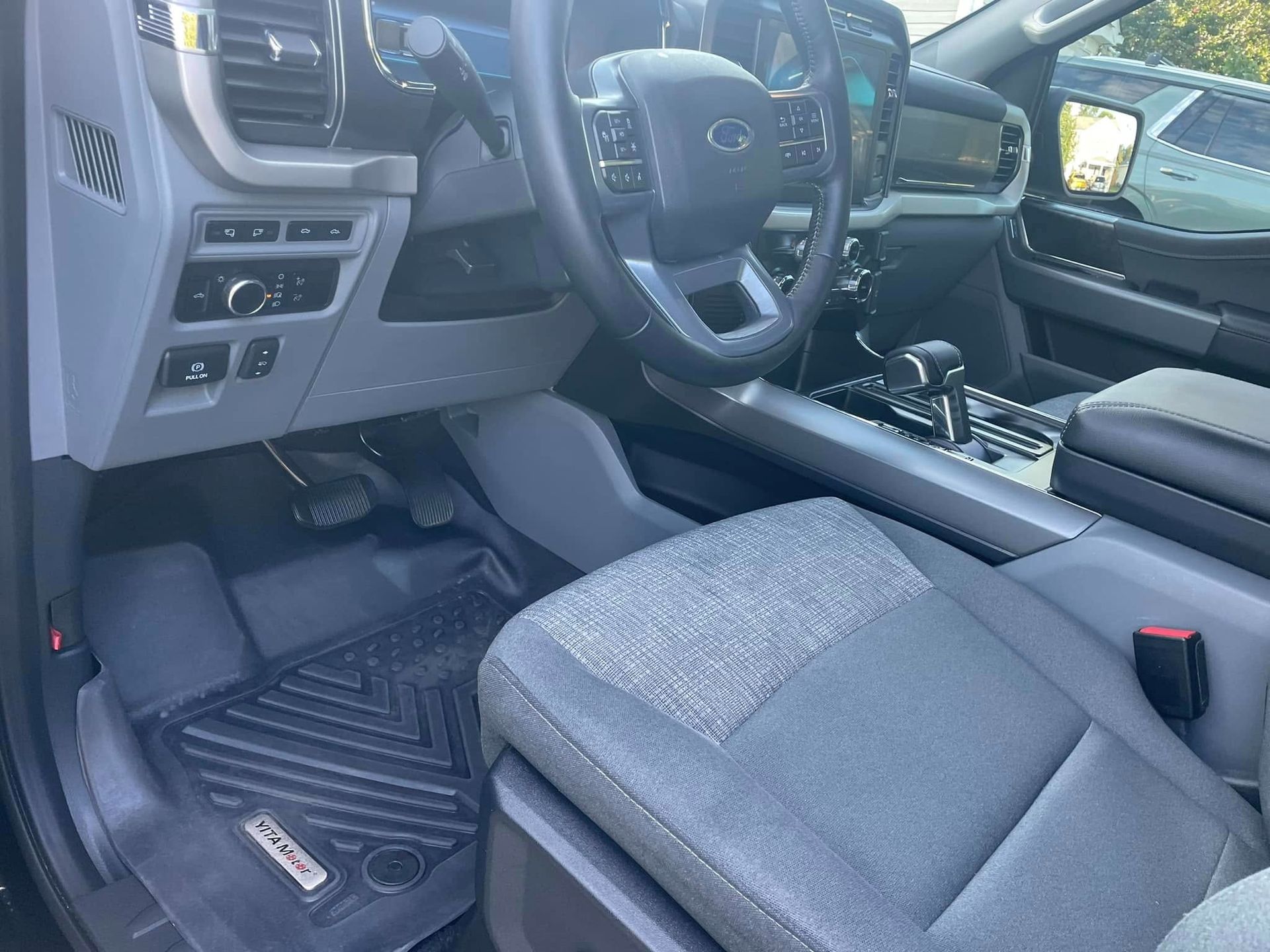 Interior of a Ford F-150 truck. Gray seats, black floor mat, steering wheel, dashboard, and gear shift.
