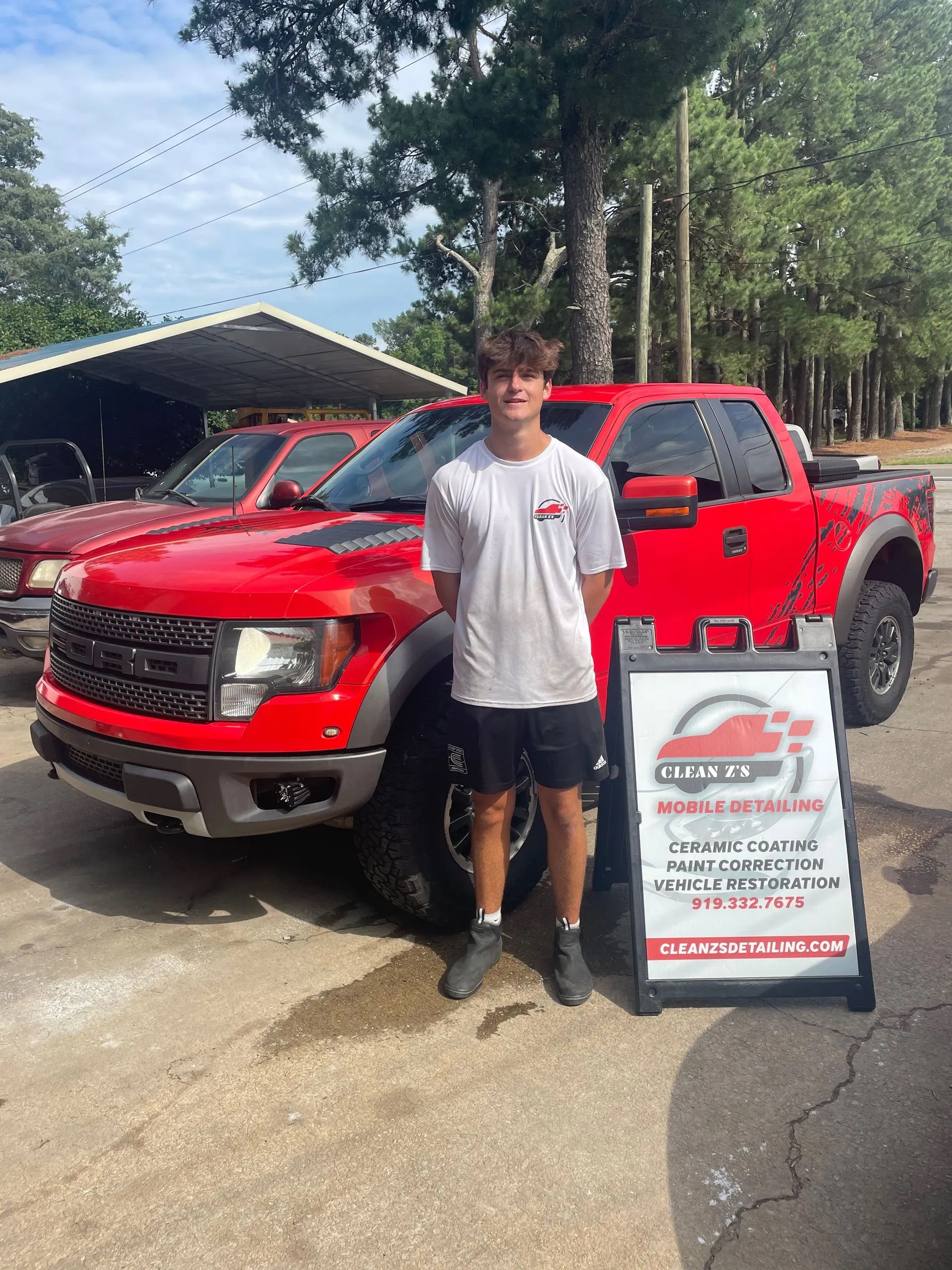 Teenager in front of a red truck, near a sign in an auto shop setting.