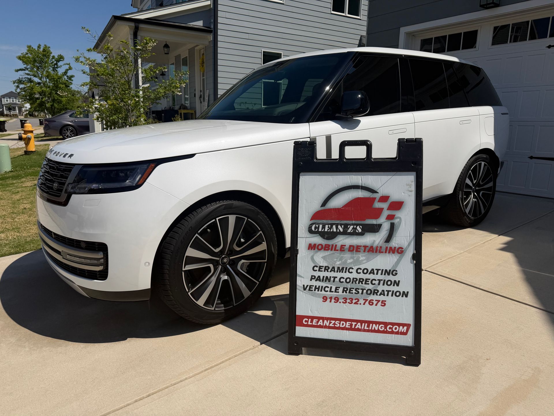 White SUV parked outside a house with a curbside carpet-cleaning service sign in front