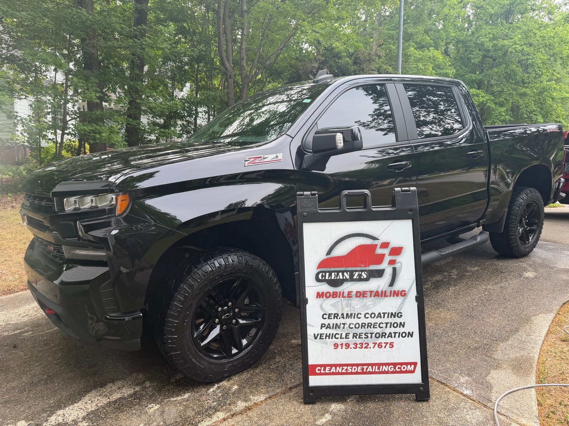 Black pickup truck beside a roadside sign advertising detailing and mobile services outdoors