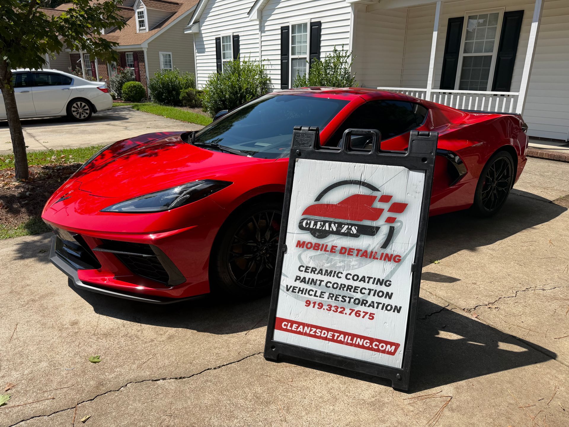 Red sports car parked by a sidewalk sign outside a house