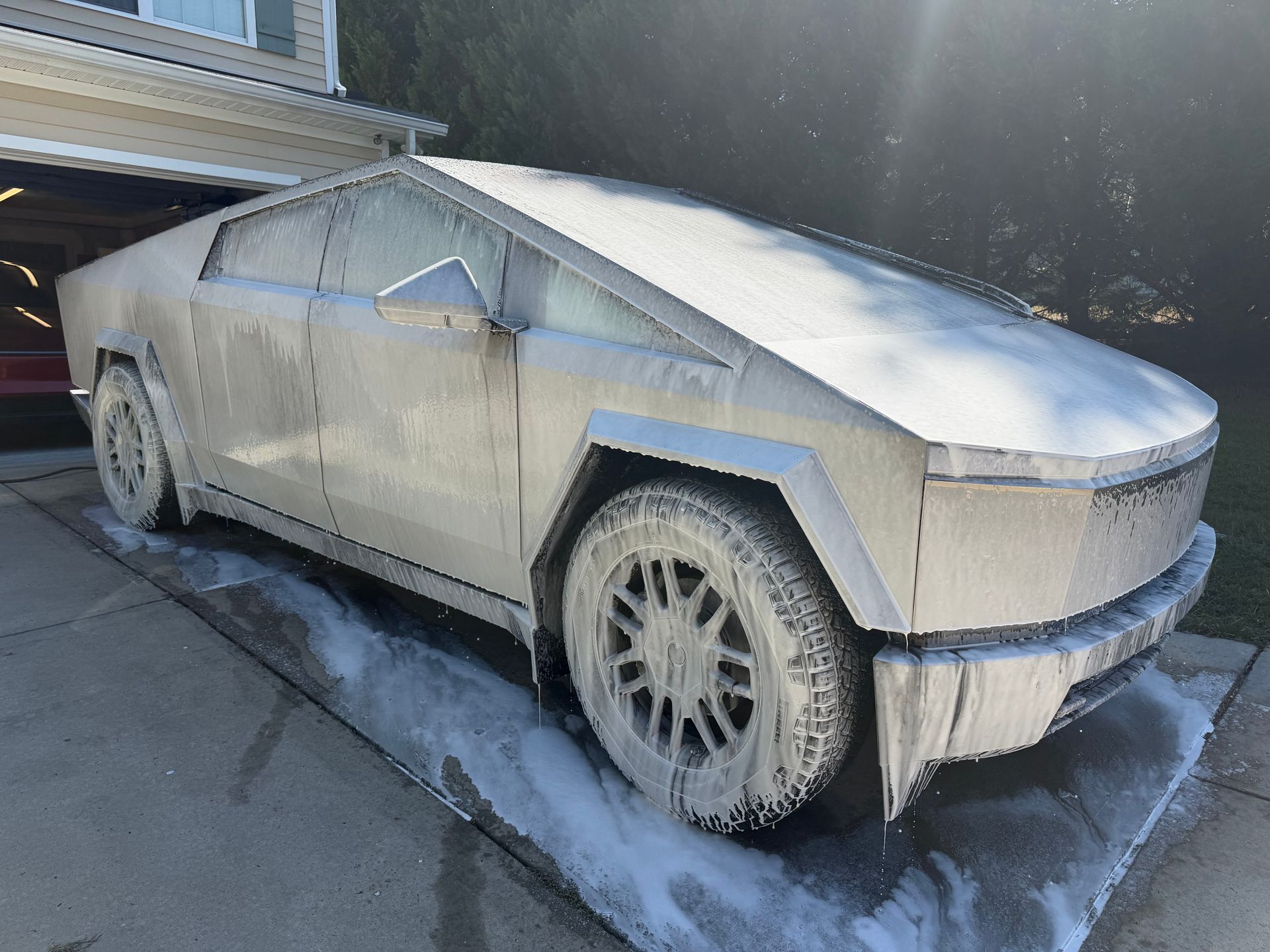 Stainless-steel Cybertruck parked in a driveway beside a house