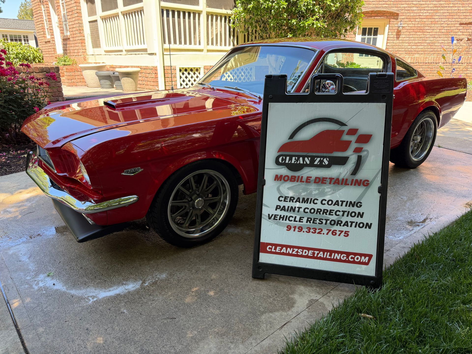 Red classic convertible beside a driveway sign advertising a cleaning service
