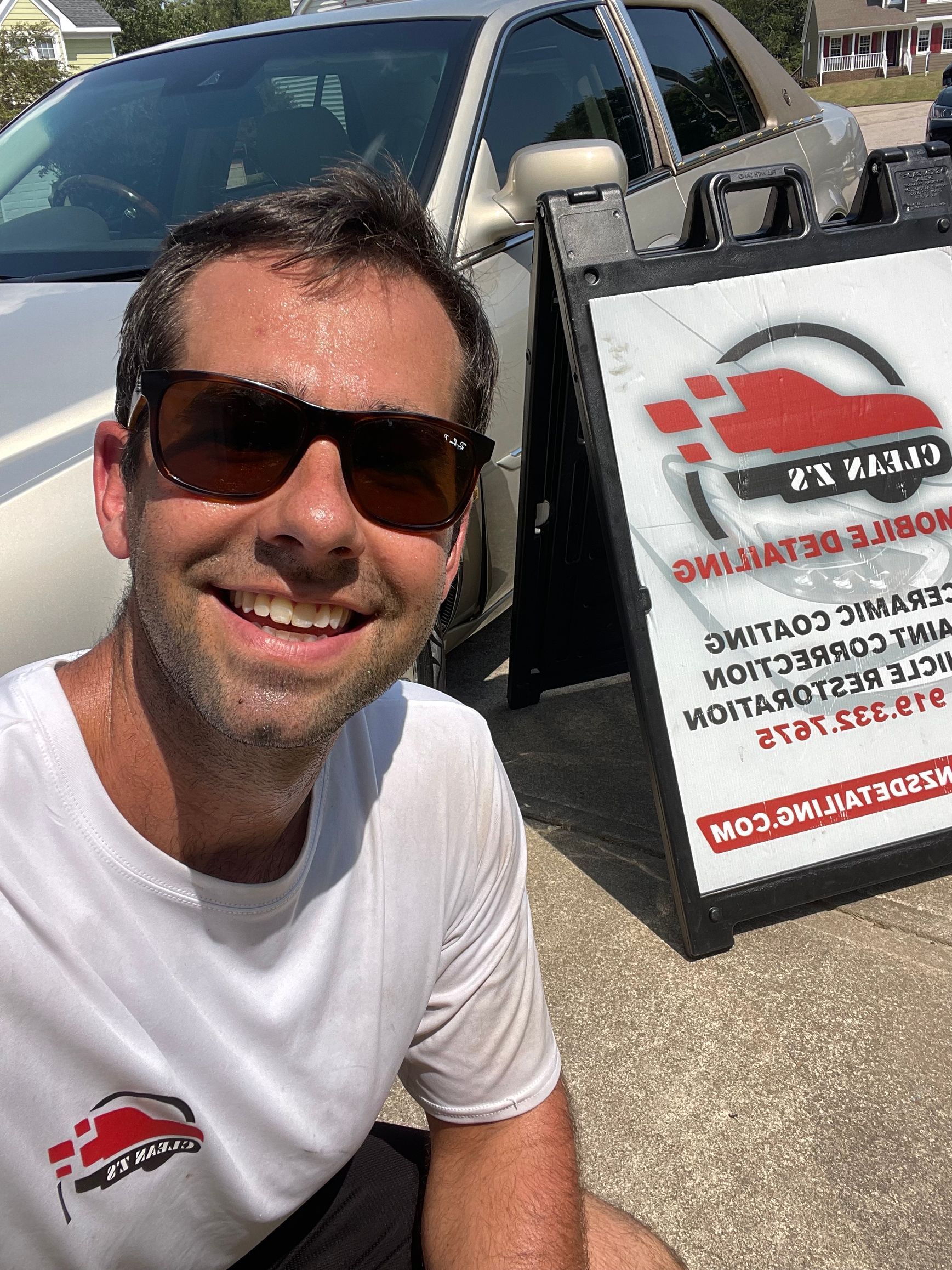 Smiling person in sunglasses beside a white service van and company sign outdoors