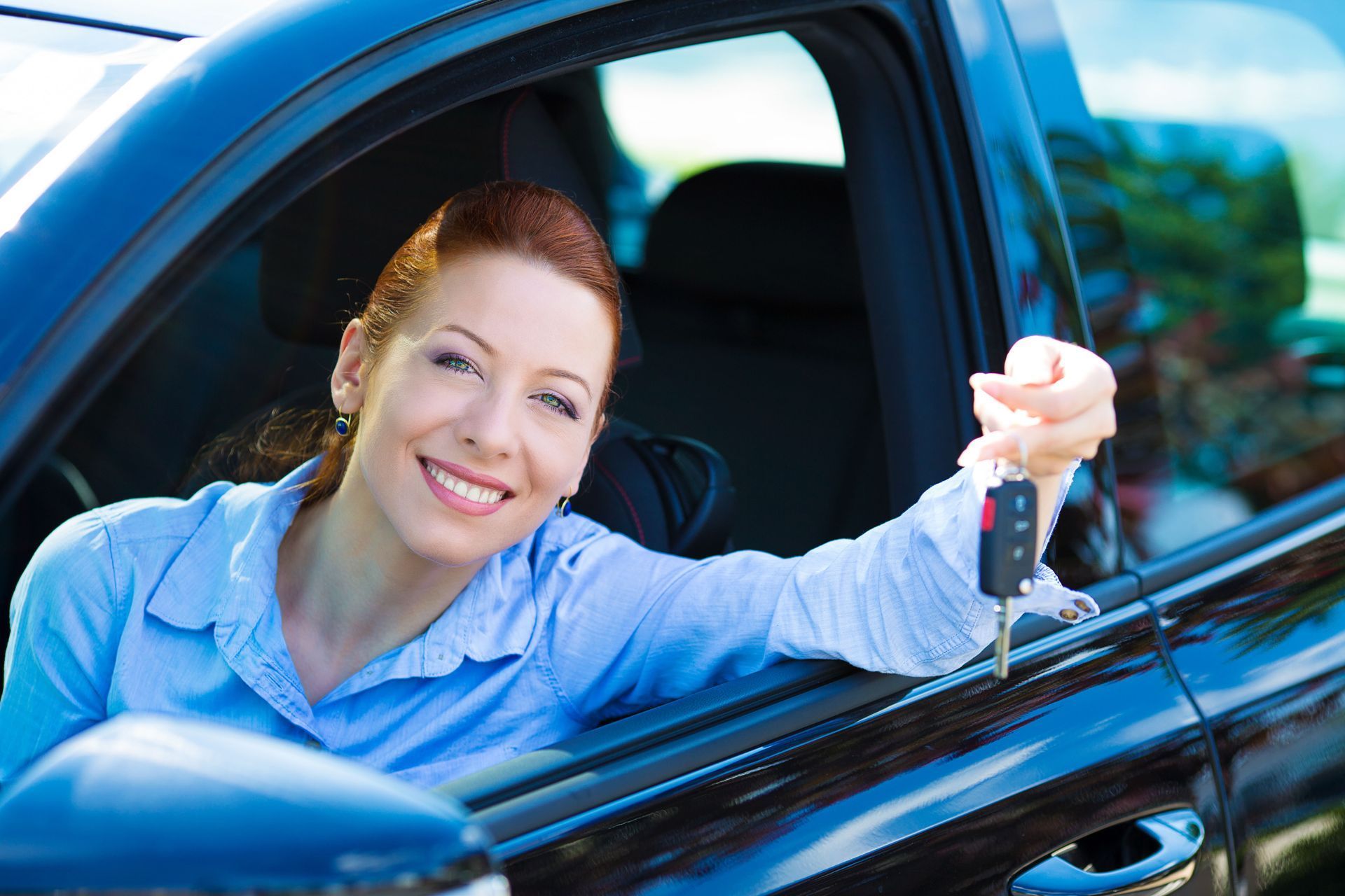 Woman in a car smiles, holding up car keys, a gesture of ownership or purchase.
