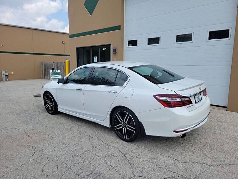 White sedan parked near a building with a closed garage door. Black and silver wheels are visible.