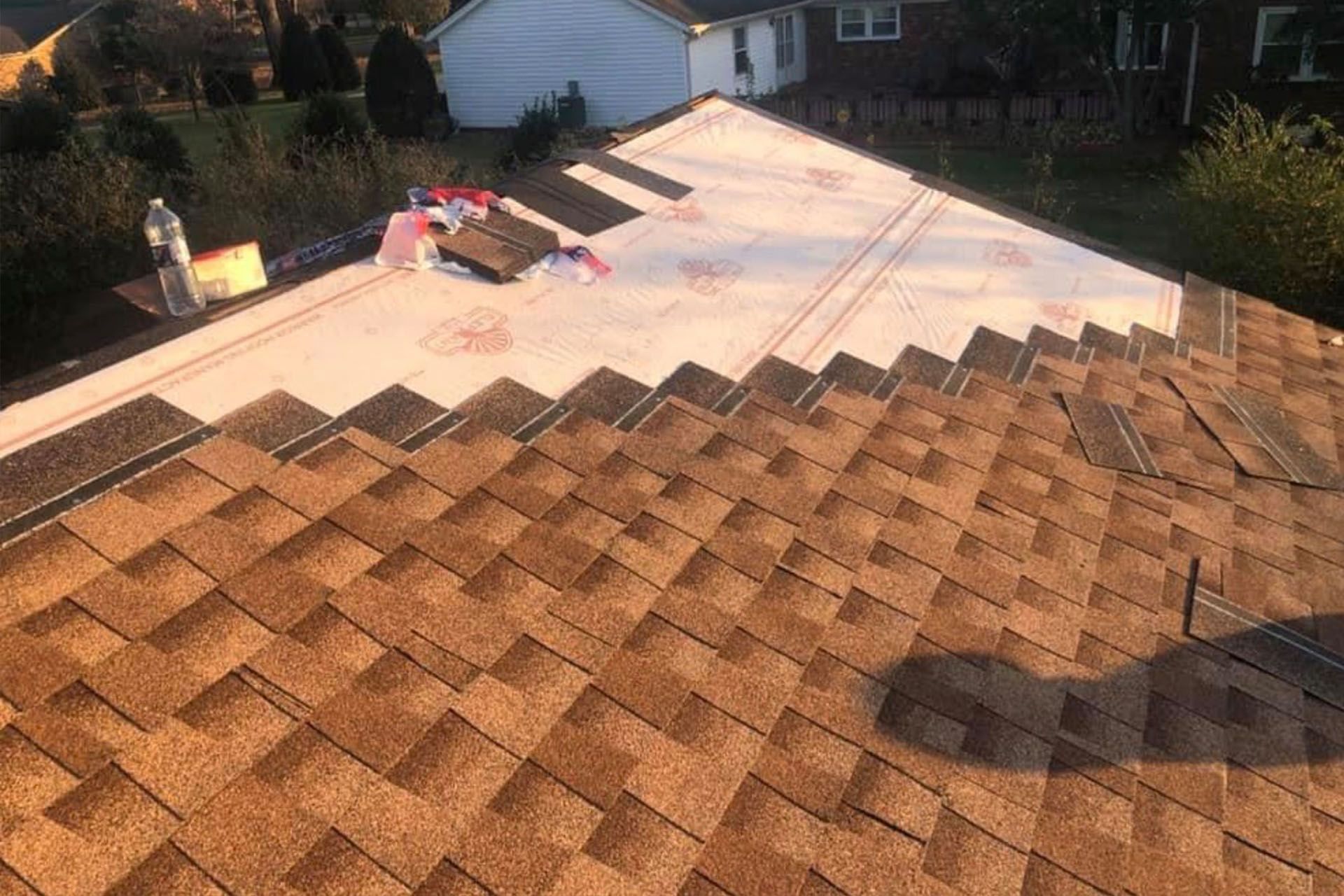 Roof partially covered with brown shingles, new roofing material visible, outdoor setting.