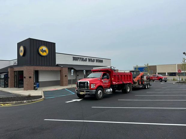 Red dump truck with trailer in a parking lot of a Buffalo Wild Wings restaurant. Cloudy sky.