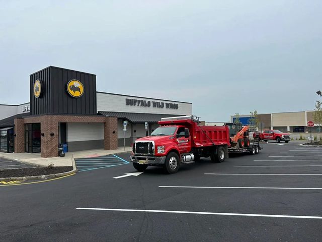 Red dump truck with trailer in a parking lot of a Buffalo Wild Wings restaurant. Cloudy sky.