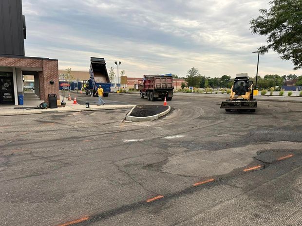 Parking lot under construction with trucks and machinery, cloudy sky.