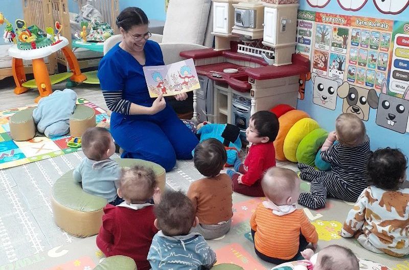 a woman is sitting on the floor reading a book to a group of babies .