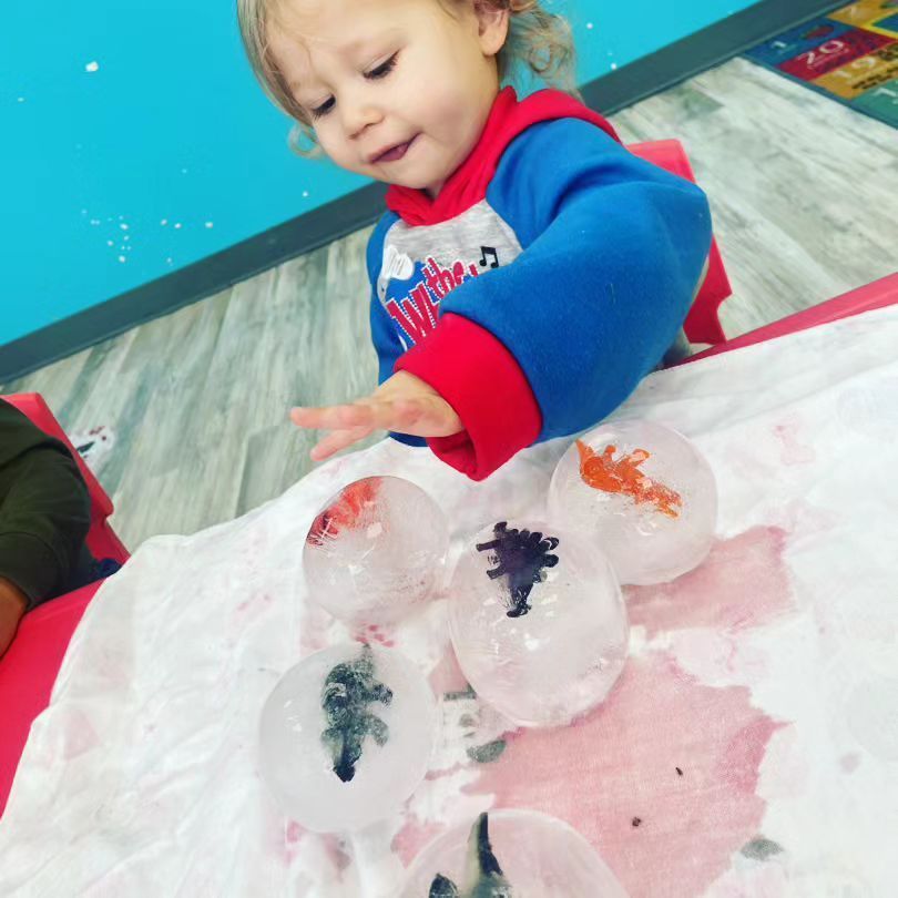 A toddler is playing with ice cubes with dinosaurs in them