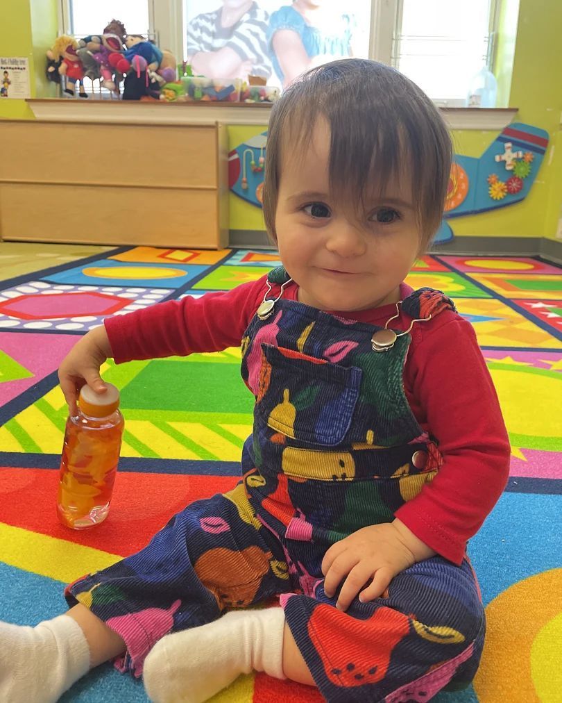 A baby is sitting on the floor holding a bottle