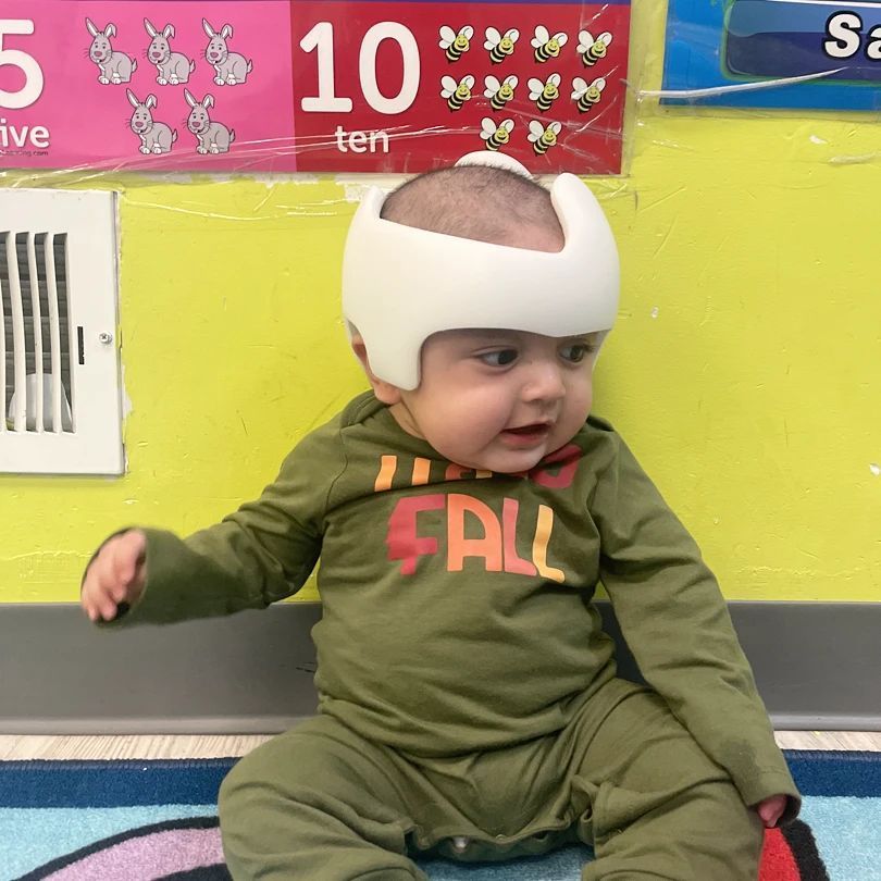 A baby wearing a helmet and a shirt that says fall
