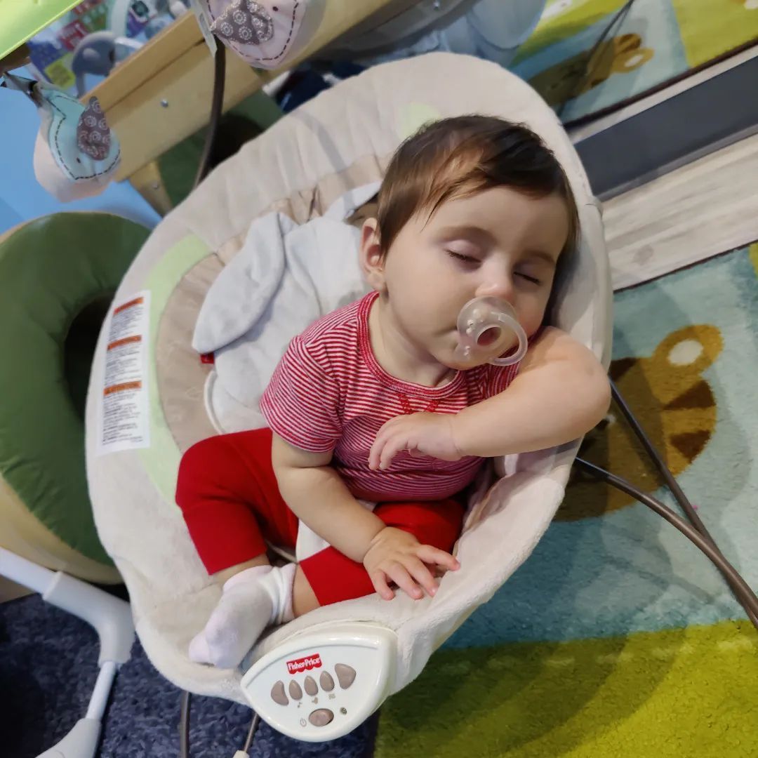 A baby is sitting in a swing with a pacifier in his mouth