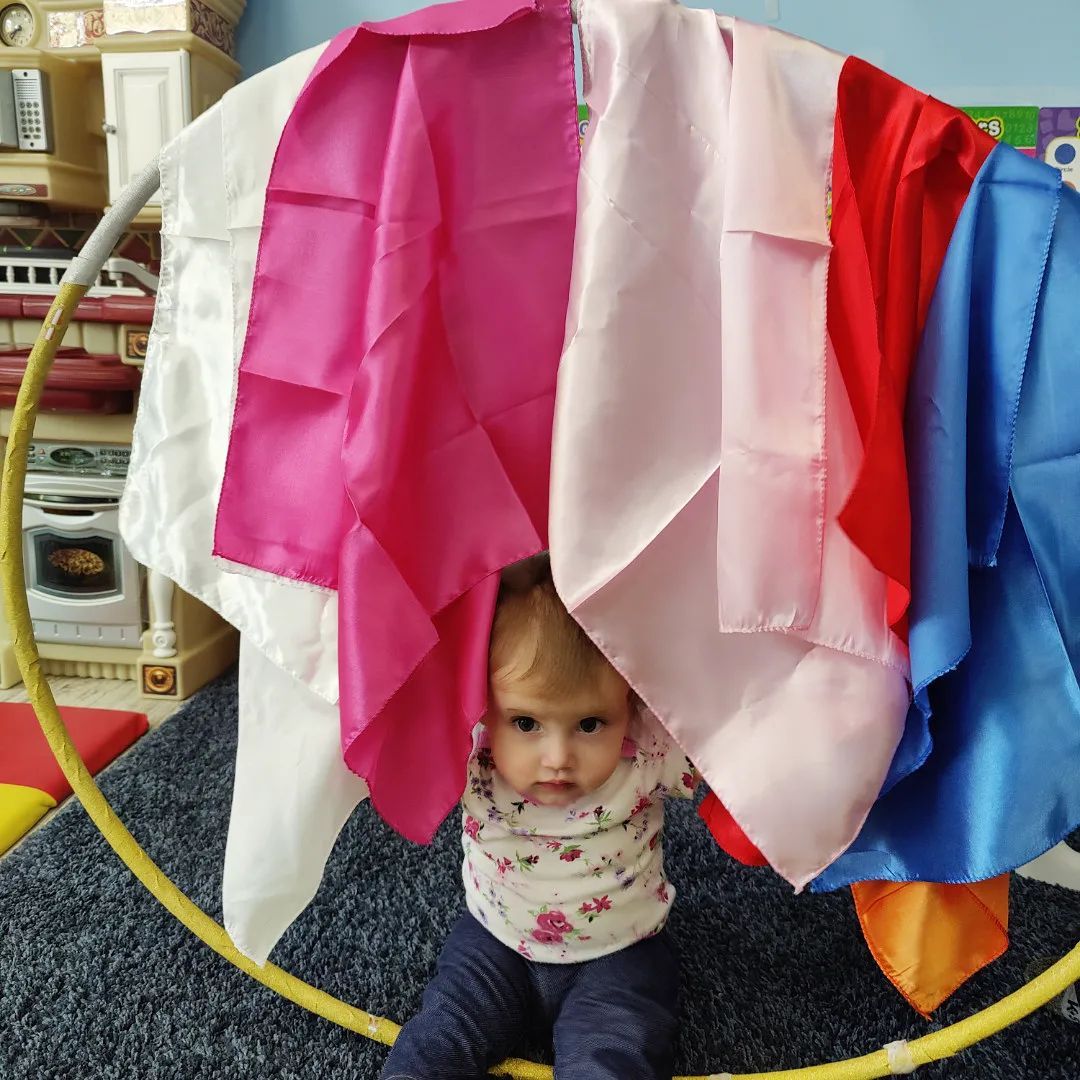 A baby is sitting under a bunch of clothes