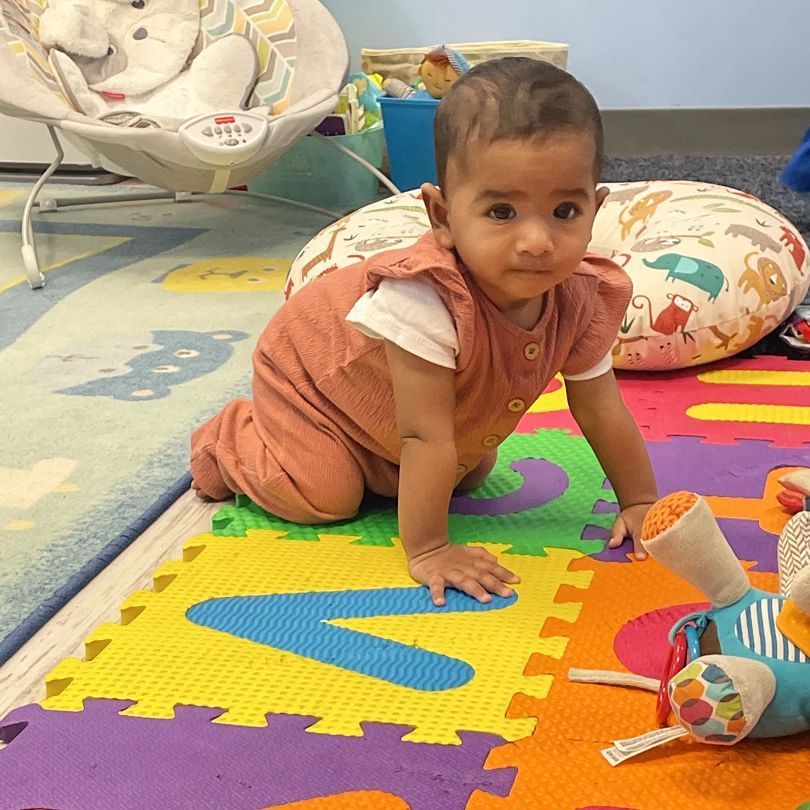 A baby is crawling on a puzzle mat with the letter v on it