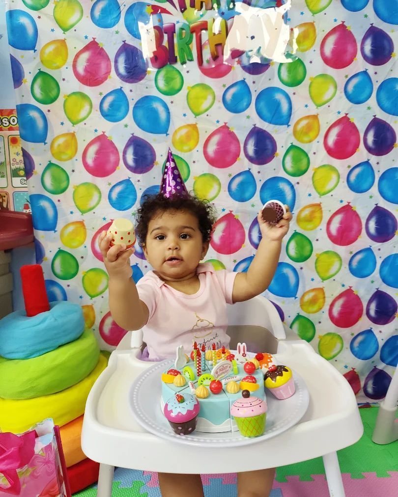 A little girl is sitting in a high chair with a birthday cake and cupcakes