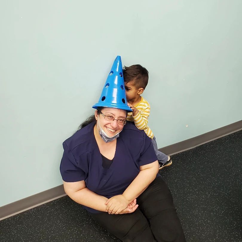 A woman wearing a blue cone hat is sitting next to a child