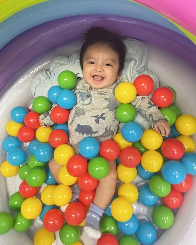 A baby is laying in a ball pit filled with colorful balls