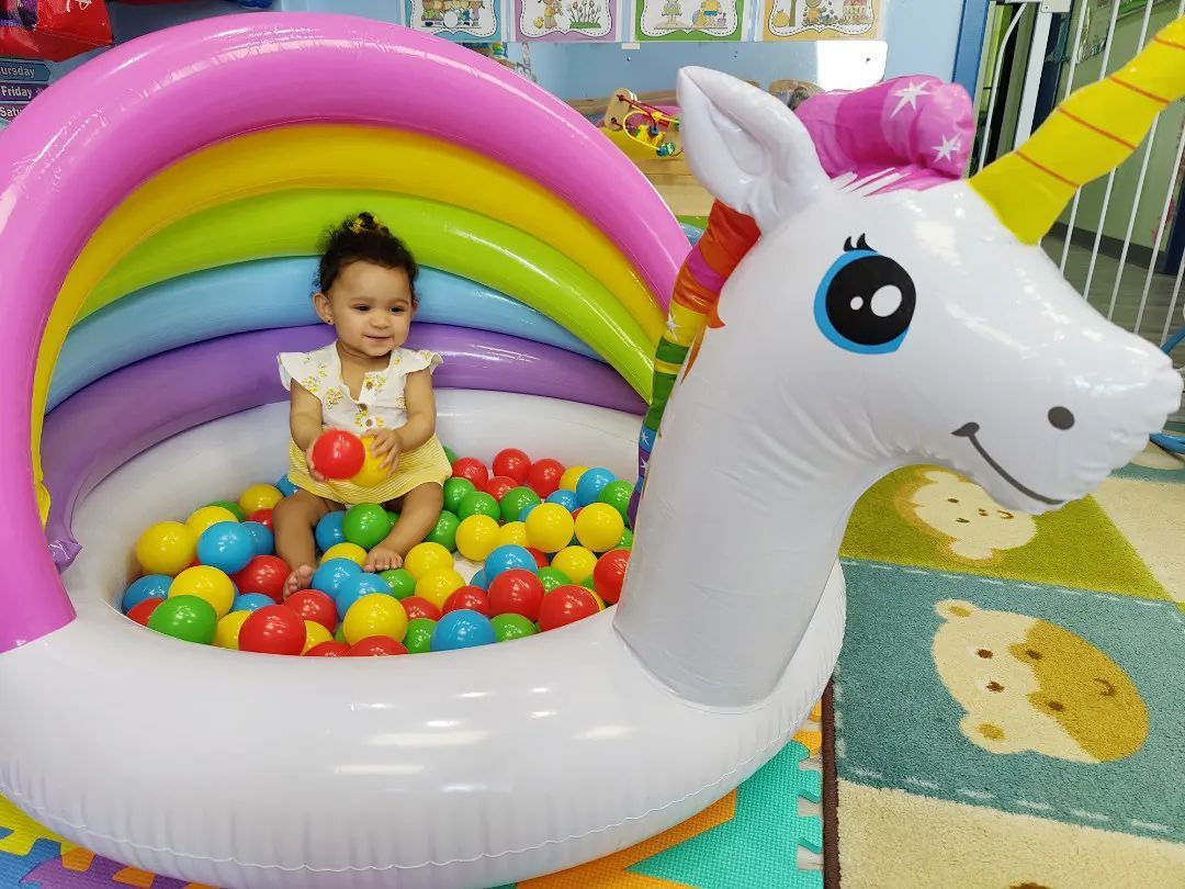 A baby is sitting in an inflatable unicorn pool filled with colorful balls